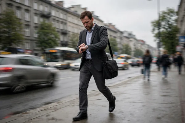Zabiegany pracownik biurowy z torbou na laptopa spieszący się ulicą w ciągu dnia.